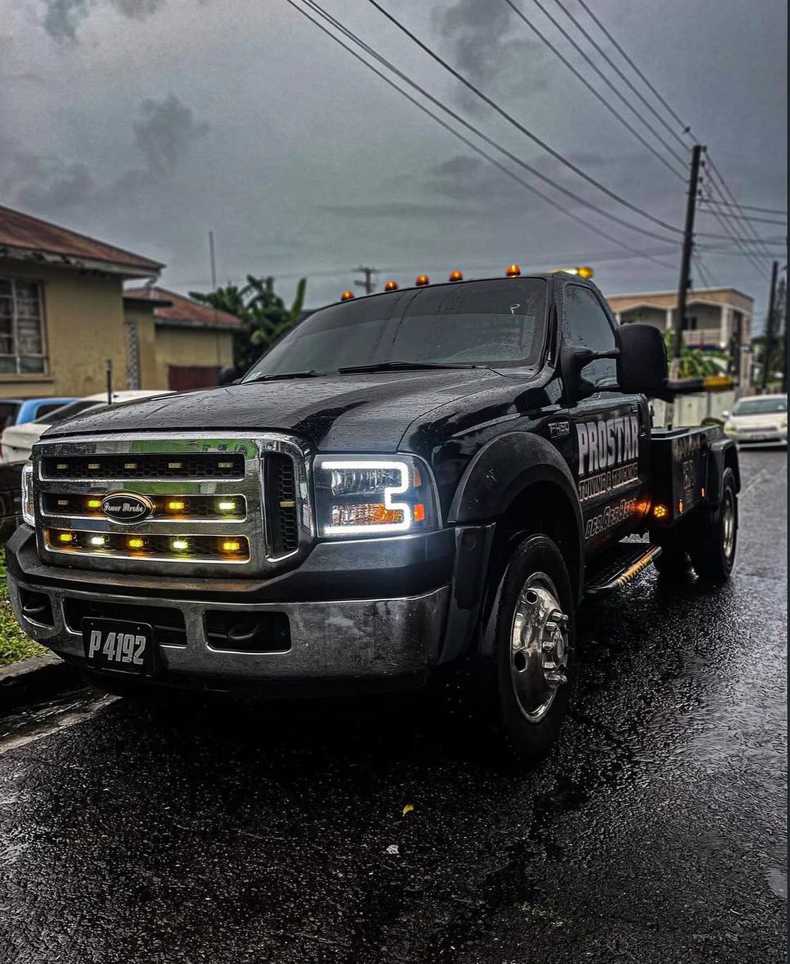 The black ProStar wrecker on a wet street at dusk with its amber cab lights and grille lights glowing